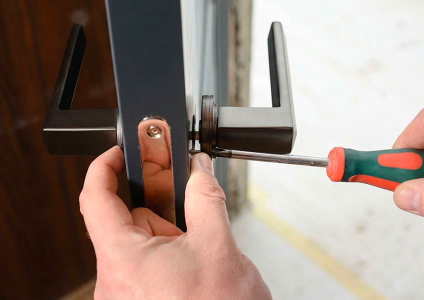 Le gros plan des mains de l'artisan avec le tournevis sur la serrure/poignée